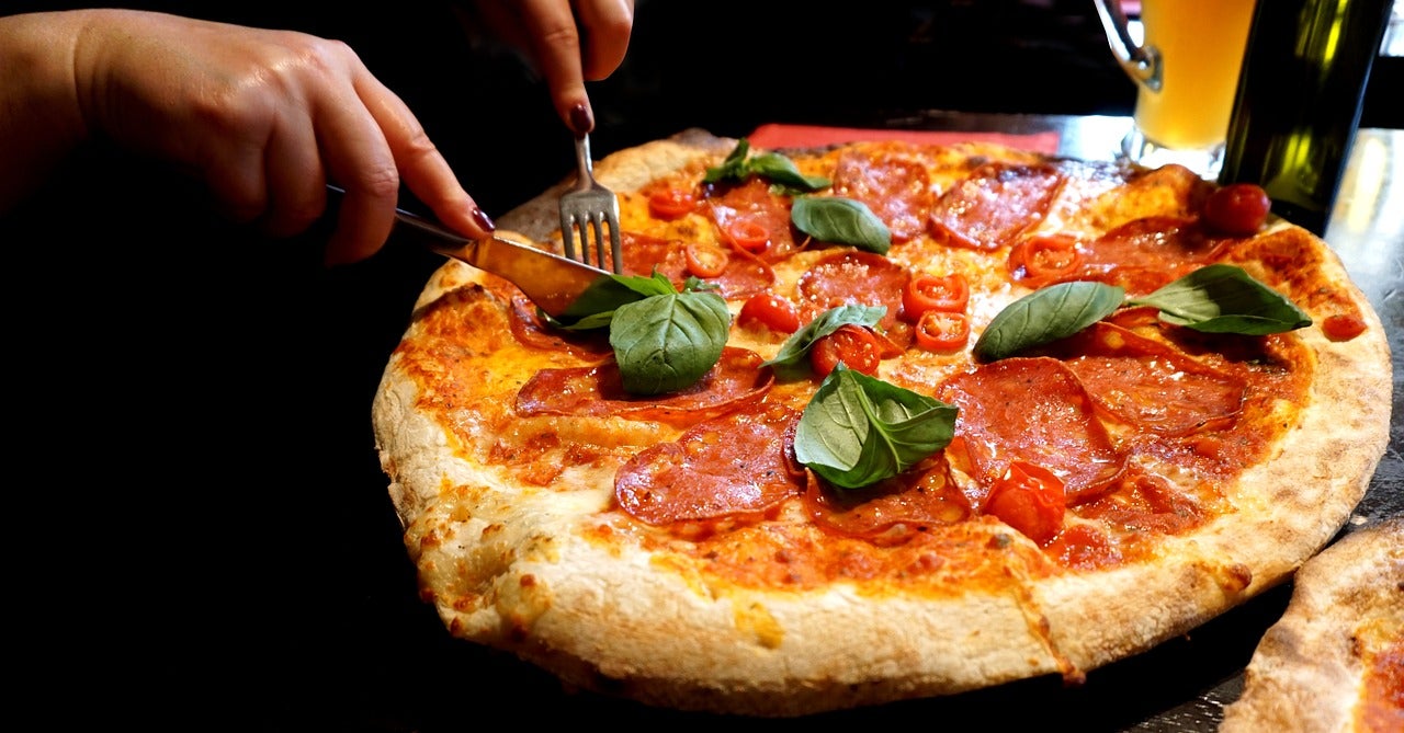 Una persona tallant un tros d'una pizza | Pixabay